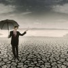 Businessman with umbrella standing on cracked earth waiting for the rain